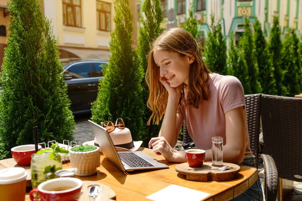 Mujer joven usando el ordenador portátil en una cafetería en una terraza de verano —  Fotos de Stock