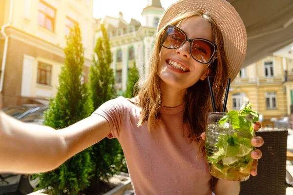 Młoda kobieta pije koktajl mojito na tarasie kawiarni w gorący letni dzień i robi zdjęcie selfie — Zdjęcie stockowe