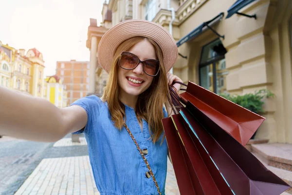 Alışveriş çantalı genç bir kadın yaz gününde şehirde selfie çekiyor. — Stok fotoğraf