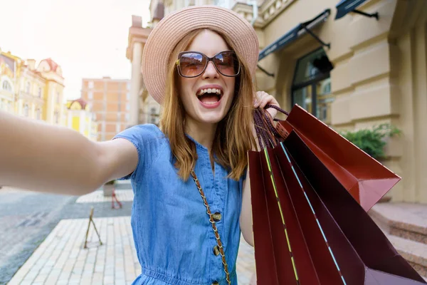 Mujer joven con bolsas de compras haciendo selfie caminar en una ciudad en el día de verano —  Fotos de Stock