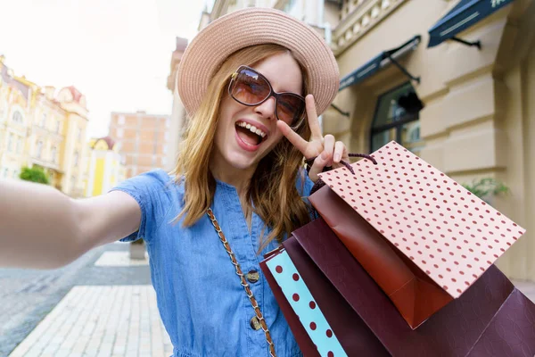 Ung kvinna med shoppingväskor gör selfie promenader i en stad på sommardagen — Stockfoto