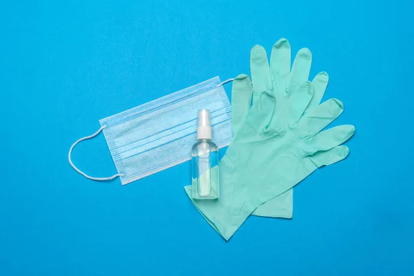 Mascarilla médica azul desechable, guantes de látex de goma y antiséptico desinfectante de manos con alcohol sobre fondo azul — Foto de Stock