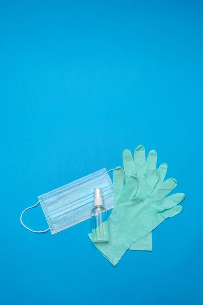 Mascarilla médica azul desechable, guantes de látex de goma y antiséptico desinfectante de manos con alcohol sobre fondo azul — Foto de Stock