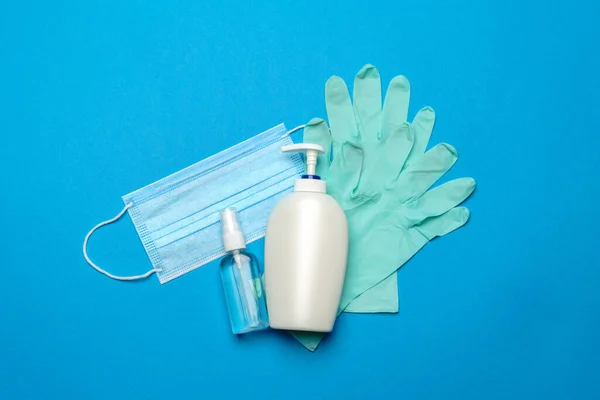 Maschera medica blu usa e getta, guanti in lattice di gomma e disinfettante mano alcol antisettico su sfondo blu — Foto Stock