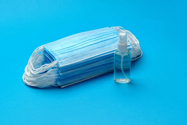 Stapel wegwerpbare blauwe medische gezichtsmaskers en alcohol hand ontsmettingsmiddel antiseptisch op blauwe achtergrond — Stockfoto