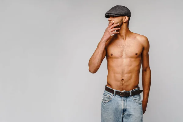 Сексуальний молодий м'язистий афроамериканський чоловік без сорочки носить шапку на світло-сірому фоні — стокове фото