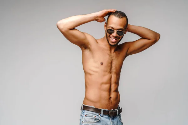 Szexi fiatal izmos afro-amerikai férfi félmeztelen visel napszemüveg felett világosszürke háttér — Stock Fotó