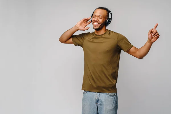 快乐的非洲男人在灰色背景下，用耳机听着音乐，面带微笑 — 图库照片