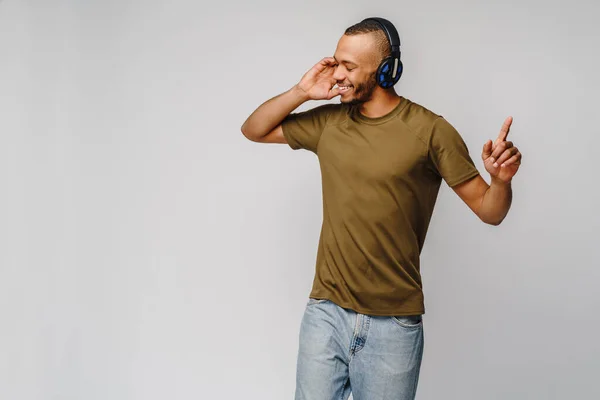 Homem africano feliz sorrindo ouvindo música em fones de ouvido sobre fundo cinza — Fotografia de Stock
