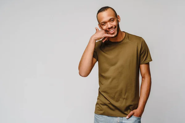 Knappe jonge Afro-Amerikaanse man toont een oproep me teken en glimlachen terwijl staan geïsoleerd op grijze achtergrond — Stockfoto
