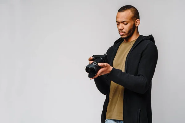 Handsome african american guy holding digital camera over light gray background — Stock Photo, Image