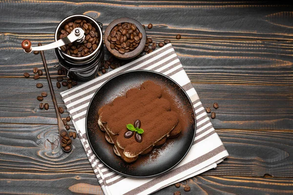 Classic tiramisu dessert and coffee grinder on ceramic plate on wooden background — Stock Photo, Image