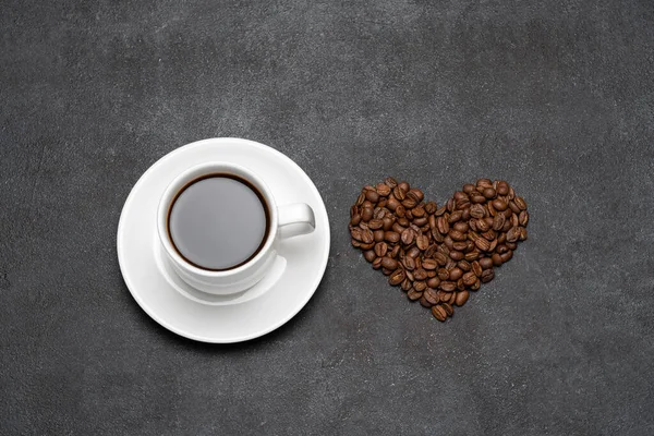 Kopje verse hete espresso koffie en hart vorm gemaakt van bonen op een donker beton — Stockfoto