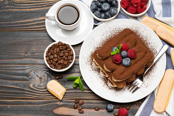 Portion of Classic tiramisu dessert with raspberries and blueberries, savoiardi cookies and cup of espresso coffee isolated on wooden background — Stock Photo, Image