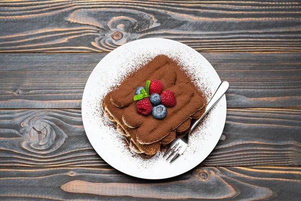 Portion of Classic tiramisu dessert with raspberries and blueberries on ceramic plate on wooden background — Stock Photo, Image