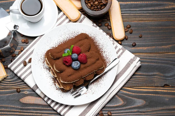 Часть классического десерта тирамису с малиной. черника, чашка эспрессо и кофеварка на деревянном фоне — стоковое фото
