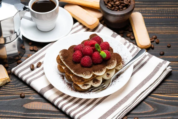 Portion klassisches Tiramisu-Dessert mit Himbeeren, Tasse Espresso und Kaffeemaschine auf Holzgrund — Stockfoto