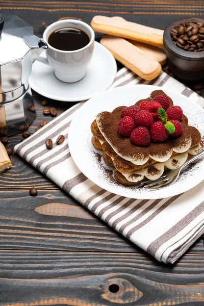 Porción de postre tiramisú clásico con frambuesas, taza de café expreso y cafetera sobre fondo de madera — Foto de Stock