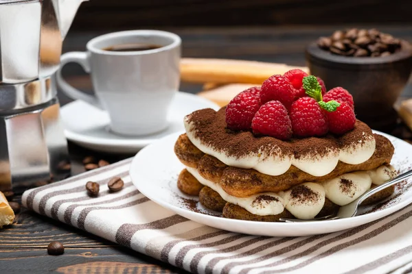 Portion klassisches Tiramisu-Dessert mit Himbeeren, Tasse Espresso und Kaffeemaschine auf Holzgrund — Stockfoto