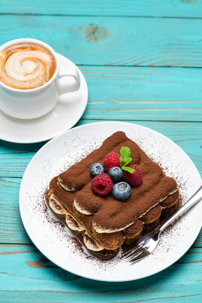 Portion of Classic tiramisu dessert with raspberries and blueberries and cup of espresso coffee on blue wooden background — Stock Photo, Image