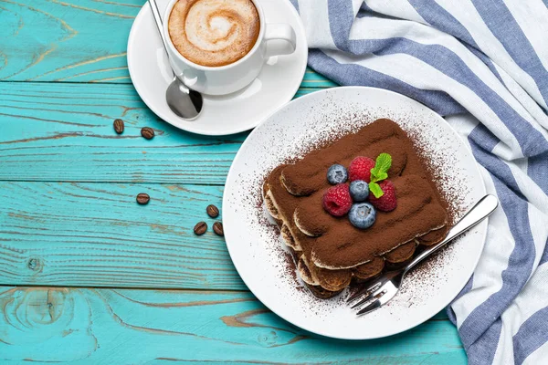 Porção de sobremesa tiramisu clássico com framboesas e mirtilos e xícara de café expresso em fundo de madeira azul — Fotografia de Stock