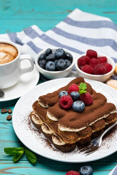 Portion klassisches Tiramisu-Dessert mit Himbeeren und Blaubeeren und einer Tasse Espresso auf blauem Holzgrund — Stockfoto