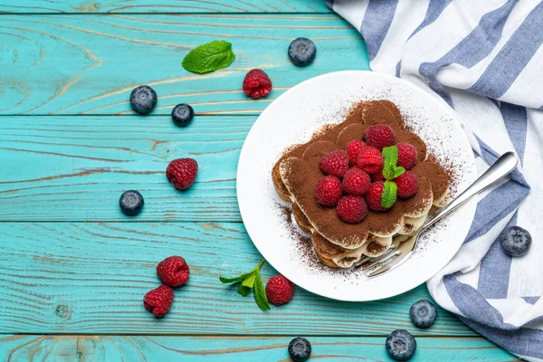 Portion klassisches Tiramisu-Dessert mit Himbeeren und Blaubeeren auf blauem Holzgrund — Stockfoto