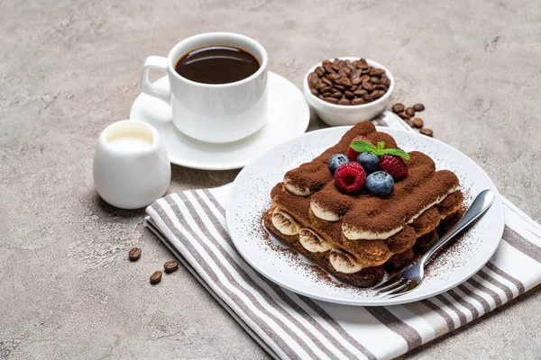 Portion klassisches Tiramisu-Dessert mit Himbeeren und Blaubeeren, Tasse Kaffee und Sahne oder Milch auf grauem Betongrund — Stockfoto