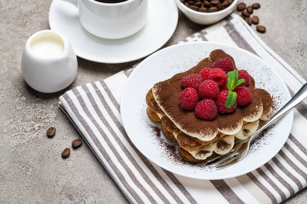 Portion de dessert tiramisu classique avec framboises et tasse de café et crème ou lait sur fond de béton gris — Photo