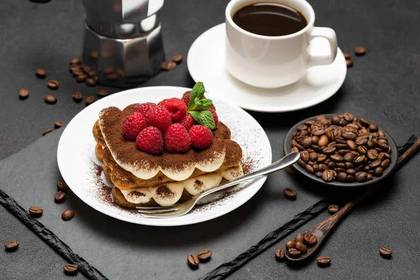 Porción de postre tiramisú clásico con frambuesas, taza de café expreso y cafetera sobre fondo de hormigón oscuro — Foto de Stock