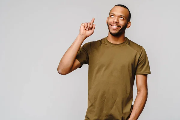 Vreugdevolle vriendelijke Afrikaans-Amerikaanse jongeman in groen t-shirt wijzend met de vinger naar kopieerruimte — Stockfoto