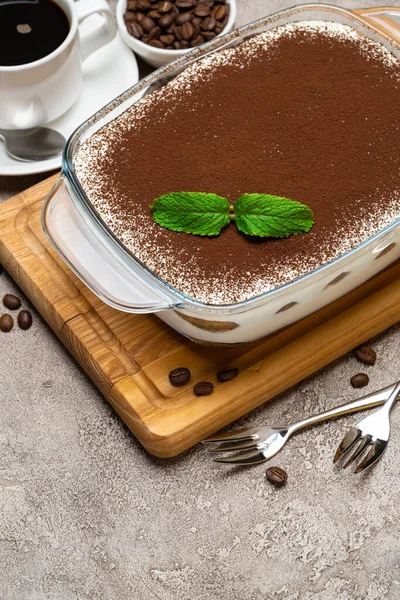 Традиционный итальянский десерт Tiramisu в стеклянной выпечке, чашка свежего кофе эспрессо и печенье savoiardi на бетонном фоне — стоковое фото