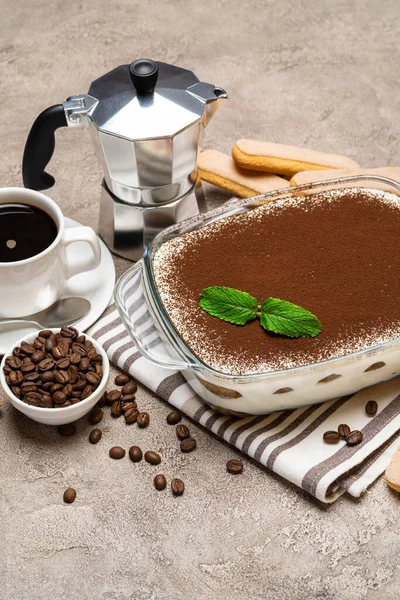 Hagyományos olasz Tiramisu desszert üveg sütő edényben, csésze eszpresszó és mokka kávéfőző beton alapon — Stock Fotó