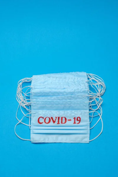 Pila de mascarillas médicas azules desechables con signo COVID-19 sobre fondo azul —  Fotos de Stock