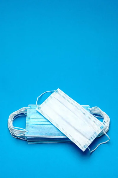 Stos jednorazowych niebieskich medycznych masek na niebieskim tle — Zdjęcie stockowe