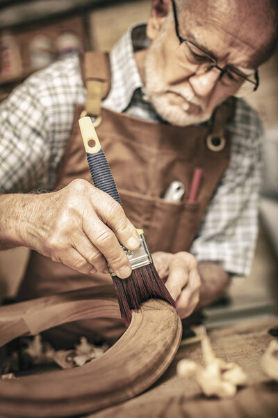 elderly carpenter uses a brush on an unfinished chair