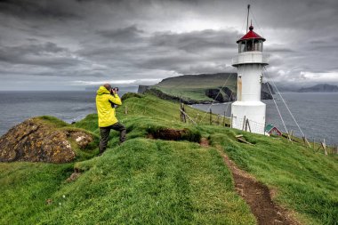 Fotoğrafçı sarı yağmurluk ile deniz feneri mykinos faroe Adaları'nda bir resim çekmek