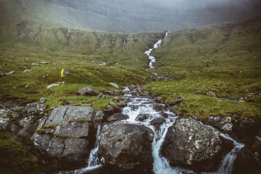 sarı yağmurluk içinde faroe şelale arayan adam
