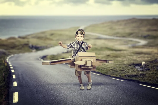孩子扮演一个飞行员与纸板飞机在孤独的道路上 — 图库照片