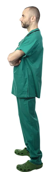 Médico de pé com uniforme verde, braços cruzados vista lateral — Fotografia de Stock