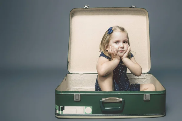 Meisje met dromerige uitdrukking zittend in een vintage koffer. — Stockfoto
