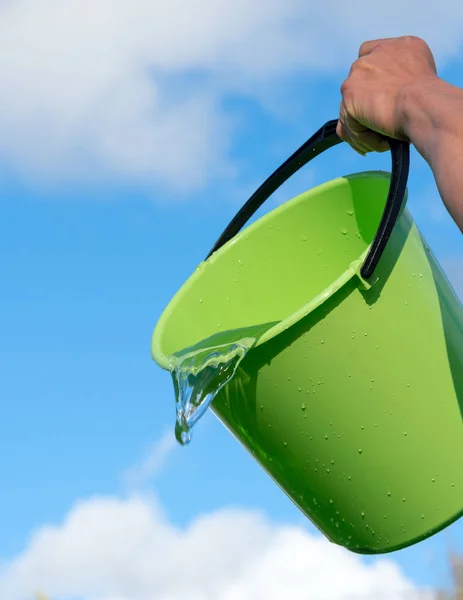 Pouring water and bucket against blue sky.