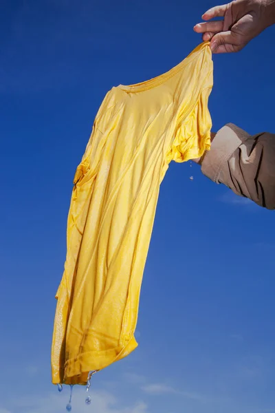 Ręka Trzyma Się Mokrej Żółta Koszulka Niebieskim Tle — Zdjęcie stockowe