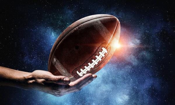Male hand on dark background and rugby ball in palm