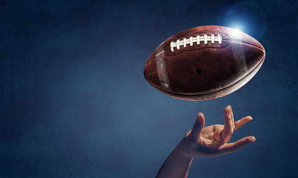Female hand on dark background and rugby ball