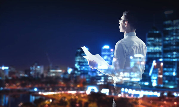 Elegant businessman with papers in hand against night city background