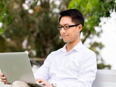 Genç işadamı açık havada otururken dizüstü bilgisayar kullanarak