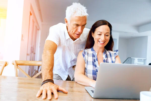 Heureux couple d'âge mûr moderne travaillant sur ordinateur portable à la maison — Photo