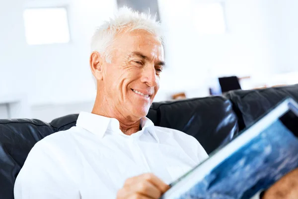 Hezký sennior muž čte knihu relaxační na pohovce — Stock fotografie