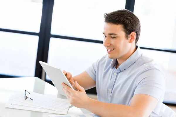 Jonge knappe zakenman met zijn touchpad zitten in kantoor — Stockfoto